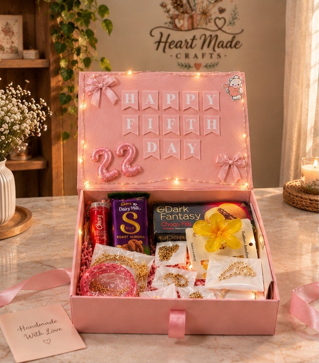 Premium customized pink gift box with fairy lights, chocolates, gold-tone jewelry, decorative flower and elegant handmade details, photographed from a front three-quarter angle.